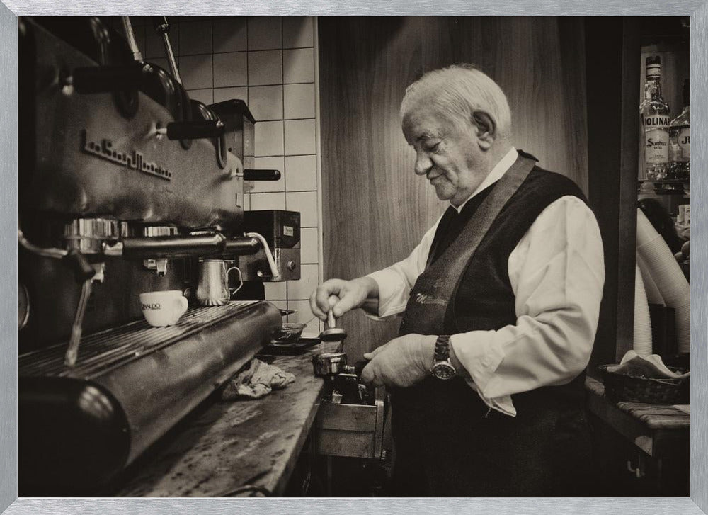 A sepia-toned, framed photograph of an elderly barista with white hair, wearing a vest, as he skillfully prepares an espresso. He is focused on his task, tamping the coffee grounds with a gentle smile, standing next to a large, vintage-style espresso machine in a cozy cafe setting. Print