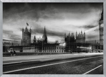 A framed, black and white long-exposure photograph of the Houses of Parliament and Big Ben in London. The view is from a bridge, with streaks of white light from traffic blurring across the road in the foreground under a dramatic, cloudy sky. Wall Art