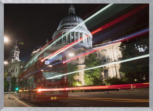 A long-exposure night photograph of a red double-decker bus in London, creating vibrant red and white light trails in front of the illuminated St. Paul's Cathedral. Decor