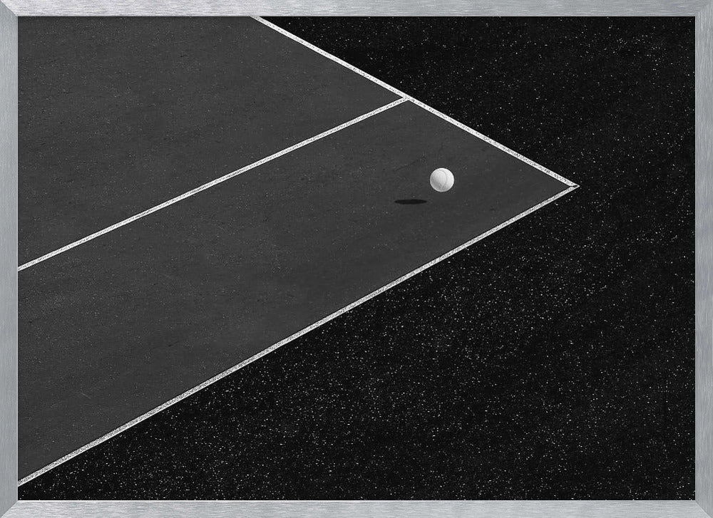 A minimalist black and white overhead photograph of a white ball resting in the corner of a dark tennis or paddle court. The composition focuses on the strong geometric angles created by the white boundary lines against the dark, textured asphalt, all within a silver frame. Artwork