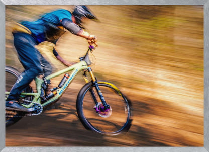 An action shot of a mountain biker in full gear speeding down a dirt trail, captured with a motion blur effect that streaks the brown and green background, conveying a sense of intense speed. Poster