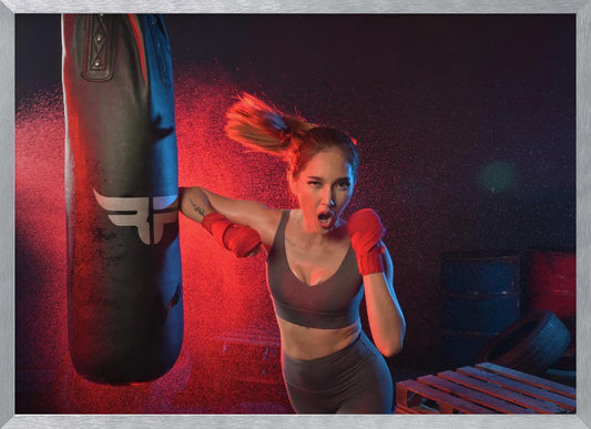 An athletic woman with her hair in a ponytail and red hand wraps fiercely punches a black heavy bag, her mouth open mid-shout. The scene is dramatically lit with red and blue light, and water droplets spray through the air from the impact. Poster