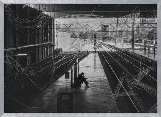 A framed, high-contrast black and white photograph of a person sitting alone on a deserted train platform, with tracks stretching into the distance. The entire scene is overlaid with frenetic white scribbles, creating an abstract and moody effect. Artwork