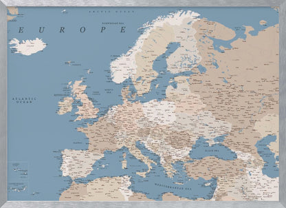 A detailed, framed map of Europe with a muted color palette. The oceans and seas are a soft blue, while the countries are various shades of beige and tan. Text labels for countries, cities, and bodies of water are clearly visible across the map. The map is housed in a simple silver-gray frame. Poster