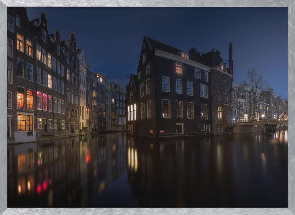 A framed photograph capturing a serene night view of an Amsterdam canal. Traditional Dutch houses with lit windows line the calm water, casting warm reflections under a deep blue twilight sky. Wall Art