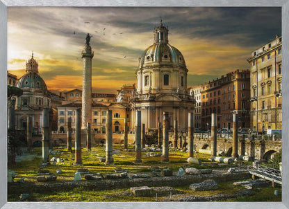 A framed photograph of Trajan's Forum in Rome, Italy, during a dramatic sunset. The foreground is filled with ancient stone columns and ruins on a grassy field, leading to the prominent Trajan's Column and the domed Church of the Most Holy Name of Mary against a golden and dark cloudy sky. Wall Art