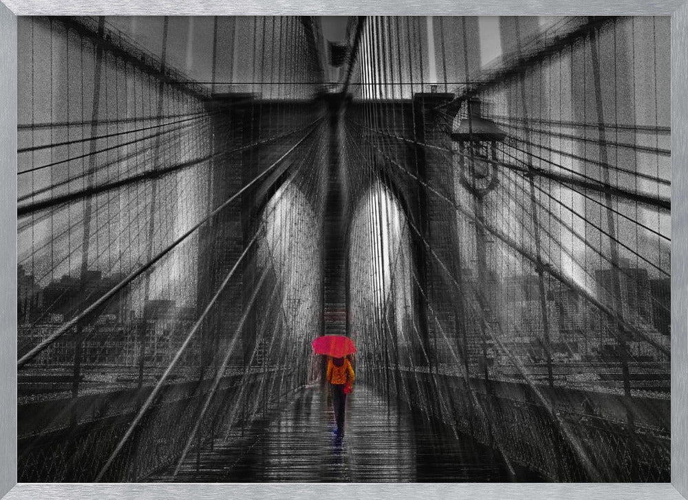 A motion-blurred, black and white photo of the Brooklyn Bridge with a person holding a bright red umbrella walking down the center. The selective color makes the red umbrella the focal point against the dramatic, almost abstract lines of the bridge's cables and arches on a wet, reflective walkway. The image is presented in a silver frame. Wall Art