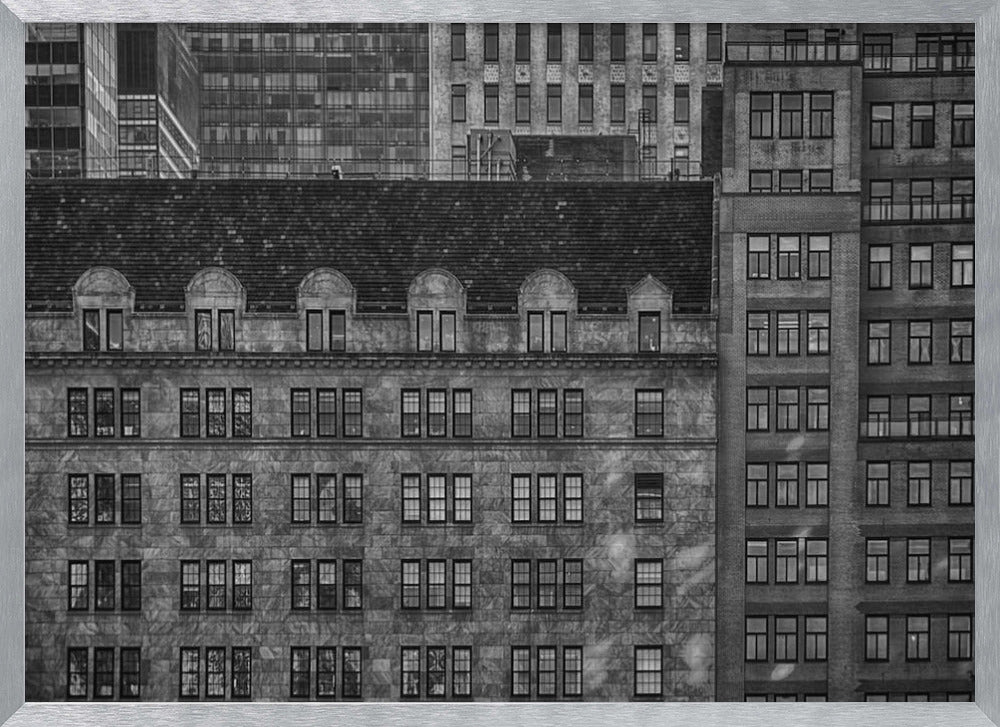A dense, black and white photograph of various city buildings packed closely together. The image highlights the contrasting architectural styles, from an older stone building with a dark roof in the foreground to taller brick and modern glass buildings in the background, creating a geometric pattern of windows and textures. Decor