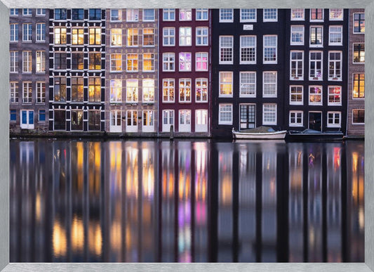 A framed photograph of colorful Amsterdam canal houses at night, their illuminated windows casting vibrant, shimmering reflections on the water below. Artwork