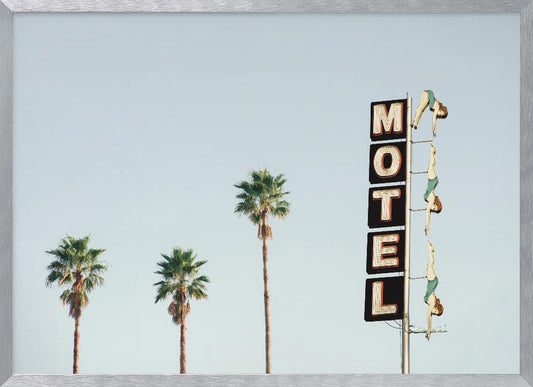 A minimalist photograph featuring three tall palm trees and a vertical black and white 'MOTEL' sign against a pale blue sky. Affixed to the sign's pole are several figures of women in green swimsuits, posed as if diving in a synchronized formation. Poster