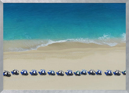 An aerial view of a pristine sandy beach with vibrant turquoise ocean waves gently lapping the shore. A long, neat row of blue and white striped beach umbrellas stands along the sand, creating a serene and orderly coastal scene, all enclosed within a silver frame. Artwork