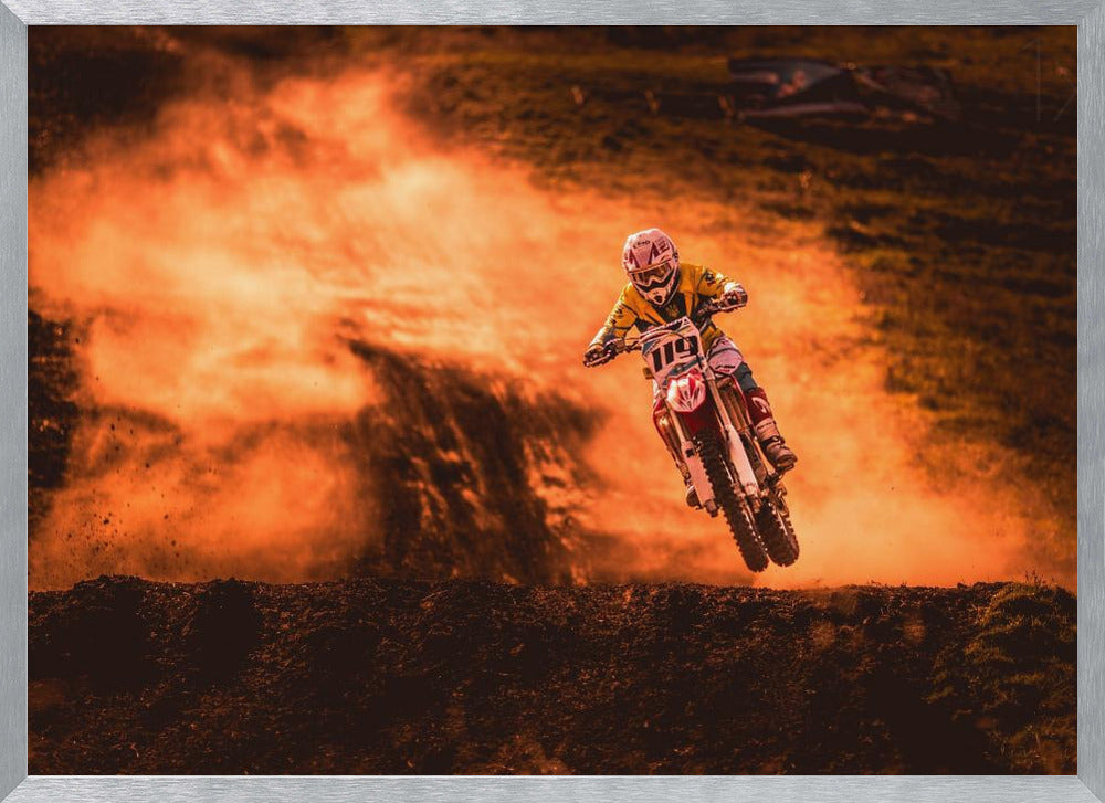 An action-packed photo of a motocross rider in mid-air, jumping their dirt bike over a mound of earth. A large cloud of orange dust billows behind them, creating a dramatic and fiery background. Wall Art