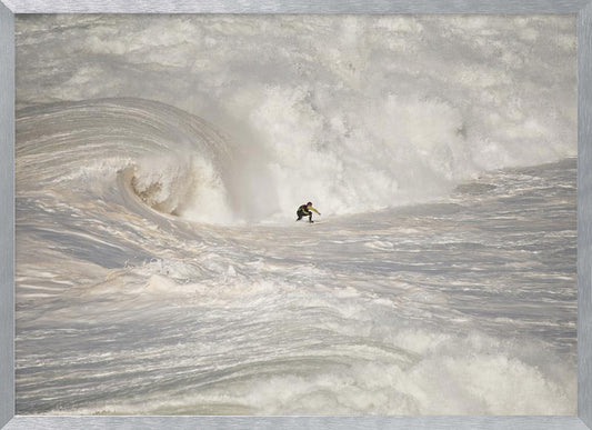 A framed photograph of a lone surfer dwarfed by a massive, powerful ocean wave. The water is a churning mass of white foam and spray, and the surfer is navigating the enormous swell. Print