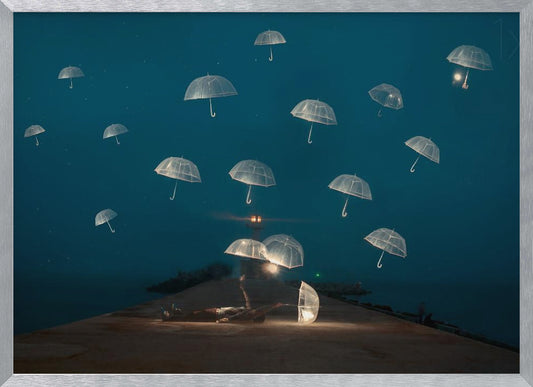 A surreal night scene with a person lying on a pier next to a glowing, transparent umbrella, while numerous other glowing umbrellas float like jellyfish in the dark blue sky above the sea, with a distant lighthouse in the background. Poster