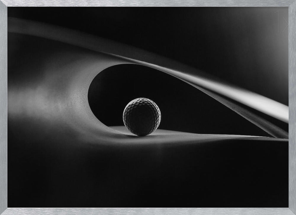 An artistic black and white photograph of a golf ball resting inside the gentle curve of a dark, abstract shape, creating a minimalist and dramatic composition with strong light and shadows. Poster