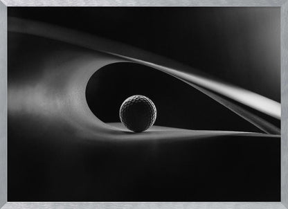 An artistic black and white photograph of a golf ball resting inside the gentle curve of a dark, abstract shape, creating a minimalist and dramatic composition with strong light and shadows. Poster