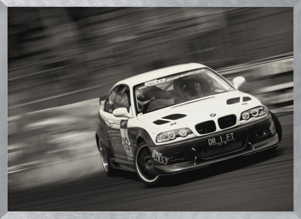 A framed, black and white action photograph of a white and black BMW race car drifting at high speed around a corner. The background is blurred with motion lines, emphasizing the car's speed as it turns, and a puff of smoke is visible from the tires. Wall Art