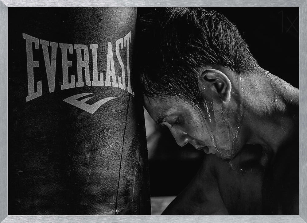 A dramatic black and white close-up photograph of an exhausted boxer resting his head against a heavy Everlast punching bag, with sweat dripping down his face and neck. Poster