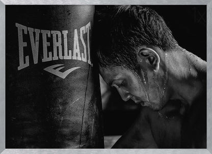 A dramatic black and white close-up photograph of an exhausted boxer resting his head against a heavy Everlast punching bag, with sweat dripping down his face and neck. Poster