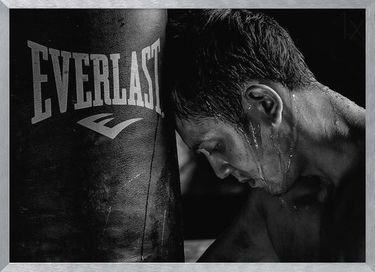 A dramatic black and white close-up photograph of an exhausted boxer resting his head against a heavy Everlast punching bag, with sweat dripping down his face and neck. Poster