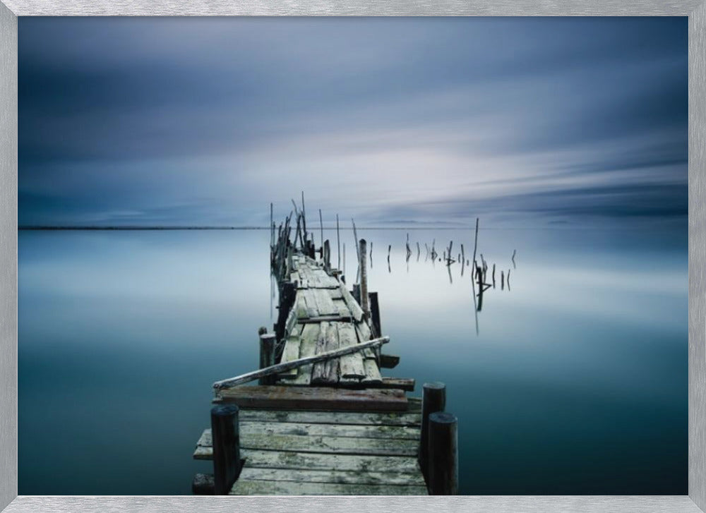 A framed, long exposure photograph of a weathered wooden pier extending into calm, misty blue water under a dramatic, cloudy sky. Wall Art