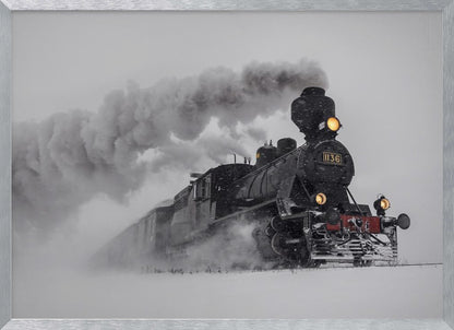 A dramatic black and white photograph of a classic steam train, number 1136, plowing through a heavy snowstorm, with its headlights glowing and a large plume of smoke trailing behind it. The image is presented within a silver frame. Print