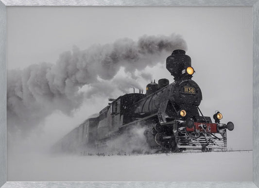 A dramatic black and white photograph of a classic steam train, number 1136, plowing through a heavy snowstorm, with its headlights glowing and a large plume of smoke trailing behind it. The image is presented within a silver frame. Print