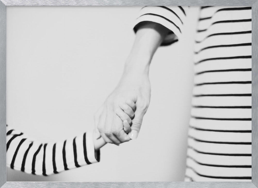 A tender black and white photograph capturing a close-up of a parent and child holding hands. Both are wearing matching striped shirts, emphasizing their connection. The image is presented in a silver frame. Print