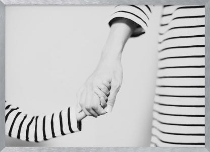 A tender black and white photograph capturing a close-up of a parent and child holding hands. Both are wearing matching striped shirts, emphasizing their connection. The image is presented in a silver frame. Print
