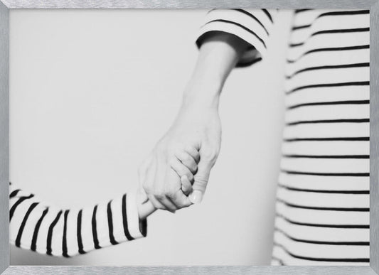 A tender black and white photograph capturing a close-up of a parent and child holding hands. Both are wearing matching striped shirts, emphasizing their connection. The image is presented in a silver frame. Print
