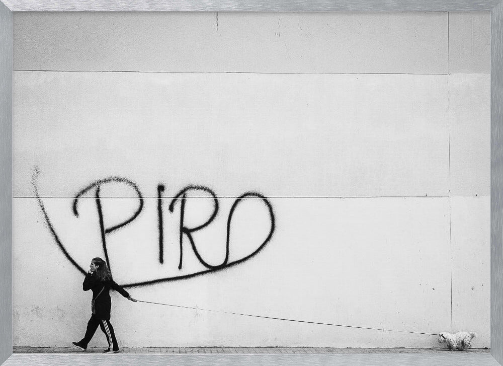 A minimalist black and white photograph of a woman dressed in black walking a small, fluffy white dog on a long leash. They are walking along a sidewalk in front of a large, pale wall with the word 'PIRO' written in black spray paint graffiti. The entire image is enclosed in a light grey frame. Poster