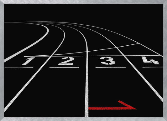 A framed, high-contrast photograph of a black running track's starting line. The lanes, marked with white lines, are numbered 1, 2, 3, and 4 and curve into the distance. A single red arrow points forward in the foreground, adding a pop of color to the monochrome scene. Poster