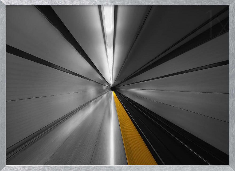 An abstract, long-exposure photograph from a first-person perspective inside a tunnel, creating a motion-blurred effect. The scene is mostly black and white, with lines radiating from a central vanishing point, but a single, bold yellow line runs down the center, adding a pop of selective color. The artwork is presented in a silver frame. Print