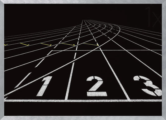 A framed, high-contrast graphic of a black running track from a low-angle perspective at the starting line. White lines delineate the lanes, with the numbers 1, 2, and 3 stenciled in the foreground. The track curves and recedes into the distance, creating a strong sense of perspective. Decor