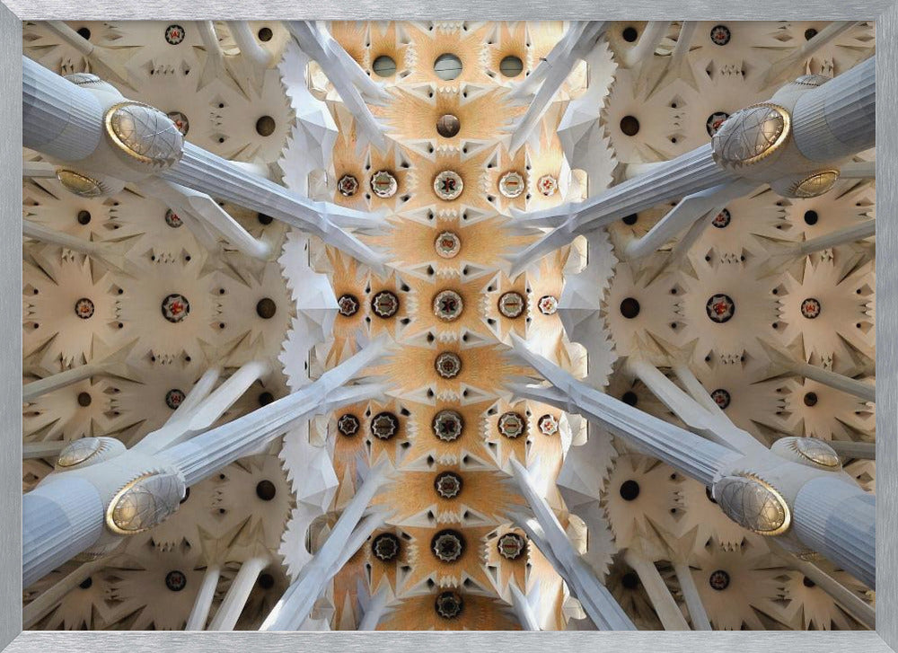A symmetrical photograph looking directly up at the ornate, geometric ceiling of the Sagrada Familia. White, tree-like columns branch out to support the intricate vaulted ceiling, which is detailed with warm orange and gold starburst patterns. Decor