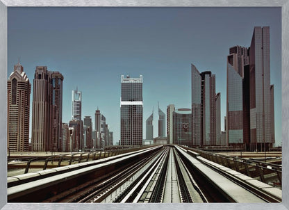 A view from an elevated train track looking down the rails towards the towering skyscrapers of a modern city skyline, under a clear, muted blue sky. Wall Art