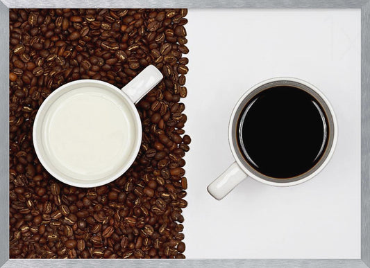 A top-down, split-screen photograph showing a contrast between coffee and milk. On the left, a white mug of milk sits on a bed of roasted coffee beans. On the right, a white mug of black coffee rests on a clean white background, creating a stark visual divide. Artwork