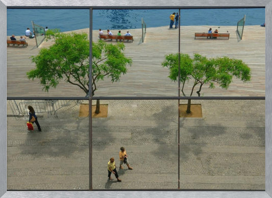 A framed, multi-pane window view showing a composite urban scene. The top panes reflect a sunny day on a wooden boardwalk by blue water, with people relaxing and green trees. The bottom panes show a direct view of a paved street below, with a few pedestrians walking. The window mullions create a grid that divides the distinct scenes. Wall Art