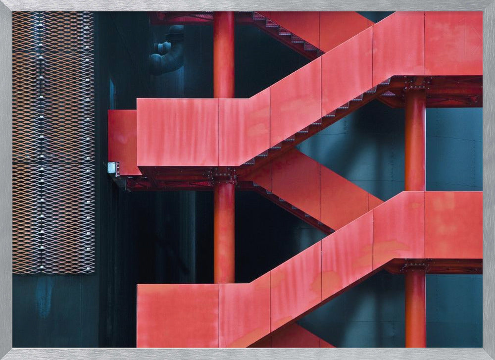 A framed abstract architectural photograph of a bright red industrial staircase zig-zagging against a dark teal wall. The composition highlights the geometric shapes and bold color contrast between the red stairs and the cool-toned background, with a silver mesh panel visible on the left side. Print