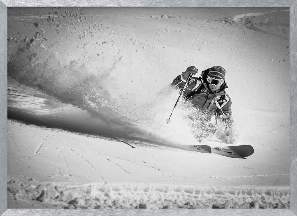 A framed, black and white action shot of a skier making a sharp turn on a snowy slope, sending a large spray of powder into the air. The skier is leaning into the turn, fully kitted out in winter gear including goggles and a beanie. Artwork