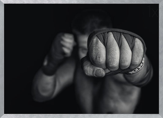 A dramatic black and white close-up photograph of a boxer's wrapped fist punching towards the camera. The fighter's body and other fist are blurred in the background, creating a powerful and intense mood. Print