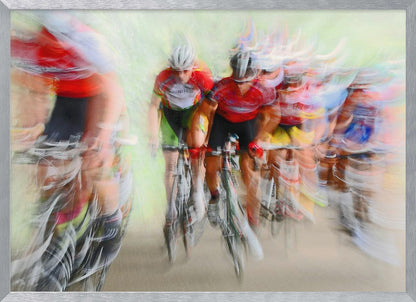 An abstract photograph of a group of cyclists in a race, captured with motion blur to create a dynamic sense of speed. The riders' red jerseys and the green background are streaked together, with a silver frame surrounding the image. Artwork