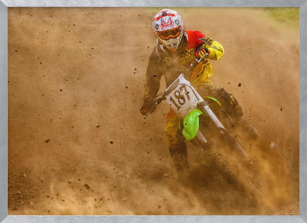 An action shot of a motocross rider in full red and yellow gear, speeding through a dirt track and kicking up a large cloud of brown dust and debris. Print