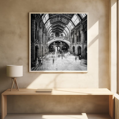 A black and white long exposure photograph of the grand hall of a natural history museum. The ornate, high-arched Romanesque architecture is in sharp focus, while a dinosaur skeleton stands in the center. Crowds of people are blurred into ghostly apparitions as they move through the vast space. Print