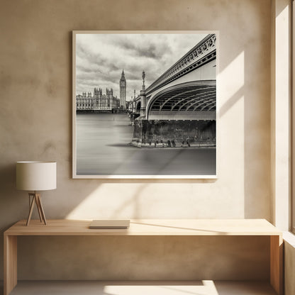 A framed, long-exposure, black and white photograph of London. The image shows Westminster Bridge from a low angle on the right, with the River Thames appearing smooth and misty. In the background on the left are the Houses of Parliament and the Big Ben clock tower under a cloudy sky. Wall Art