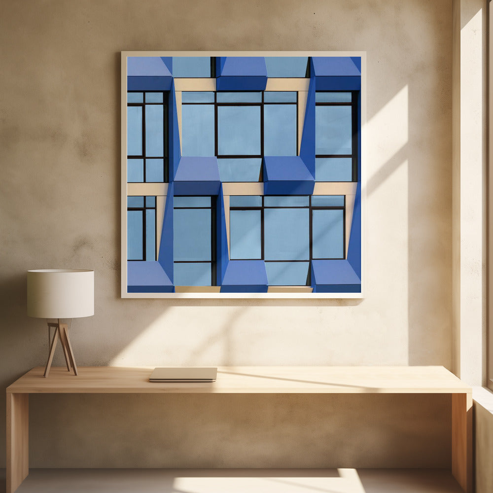 A framed abstract architectural photograph showing a repeating pattern of a modern building's facade. The image features geometric, three-dimensional blue elements surrounding light blue windows with black frames, all set against horizontal cream-colored bands. The entire piece is presented within a light wood frame. Print