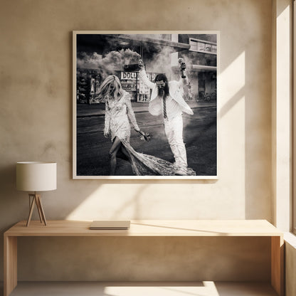 A black and white photograph in a light wood frame showing a stylish couple walking down a street. The woman wears a sparkling sequin gown, and the man, in a white suit with a long beard, triumphantly raises his arms, holding a smoke bomb and a bottle with a rose. Decor
