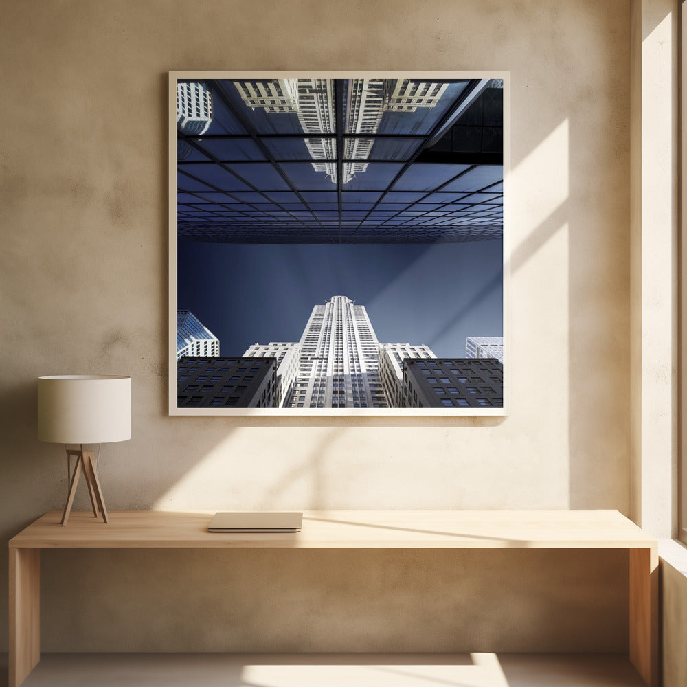 A framed, low-angle photograph capturing a stark white skyscraper against a deep blue sky, with its perfect reflection mirrored in the dark glass facade of an overhanging building, creating a surreal and symmetrical composition. Wall Art