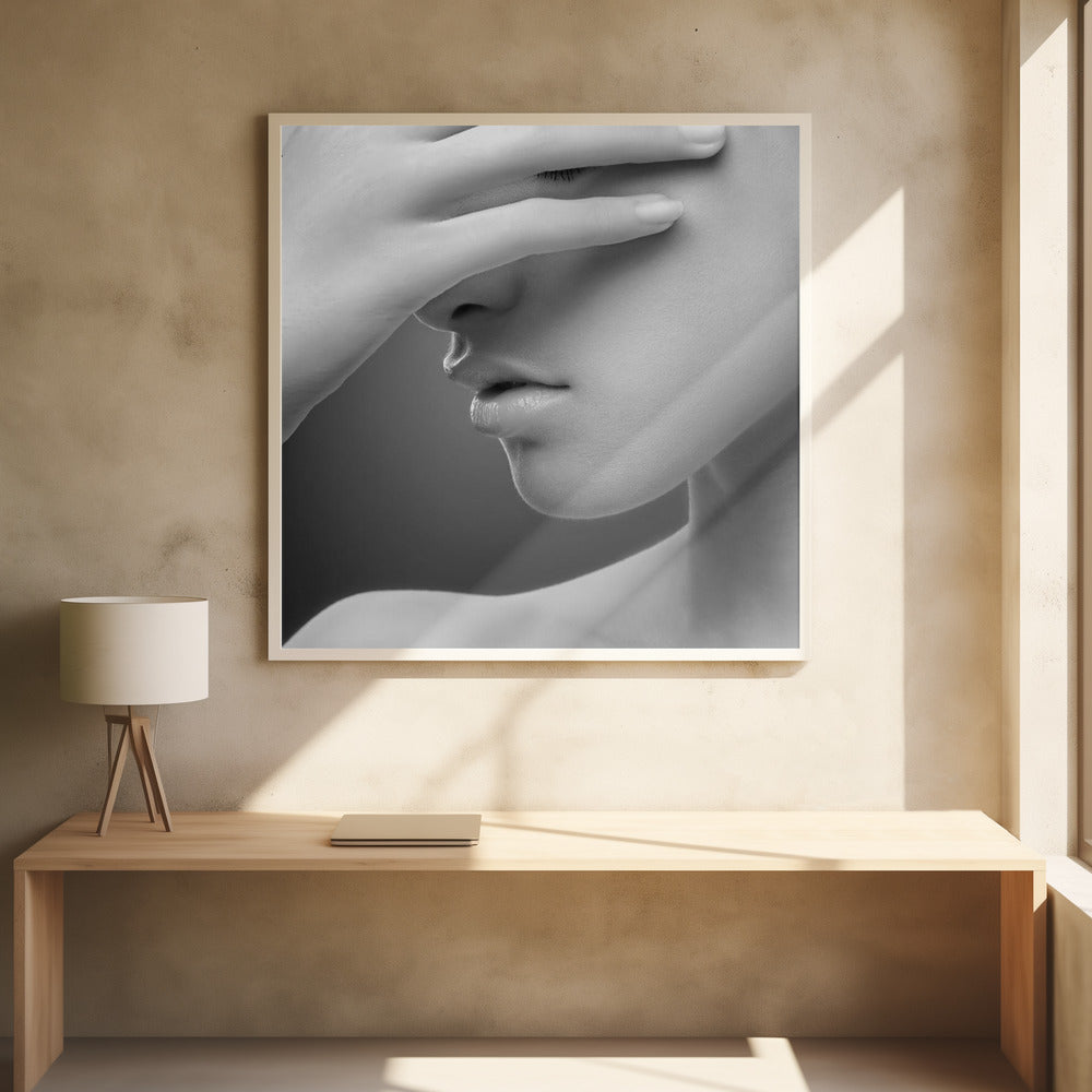 A close-up, black and white photograph of a woman's face. Her hand covers her eyes, revealing only the lower half of her face including her nose, lips, and chin. The image has a soft, sensual quality and is set within a light-colored wooden frame. Decor