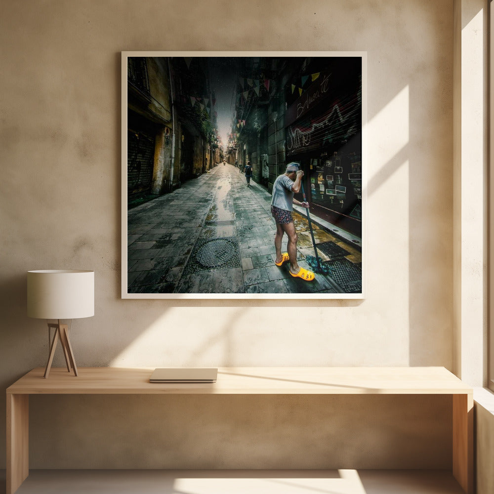 A wide-angle, atmospheric photograph of a man in bright yellow clogs mopping a wet, narrow cobblestone alley. The dark, gritty city street is lined with old buildings and closed storefronts, with another person walking in the distant light at the end of the alley. Wall Art